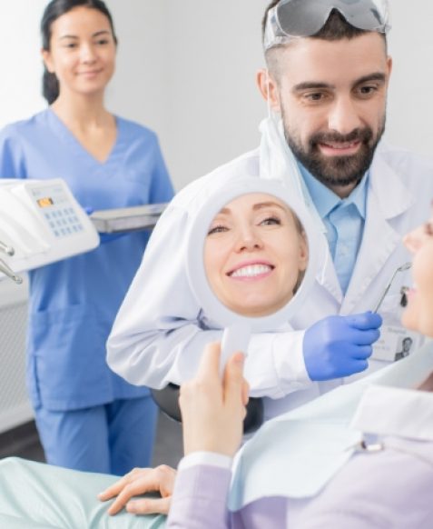 young-smiling-woman-looking-mirror-after-procedure-professional-whitening-while-sitting-armchair-dentist-office